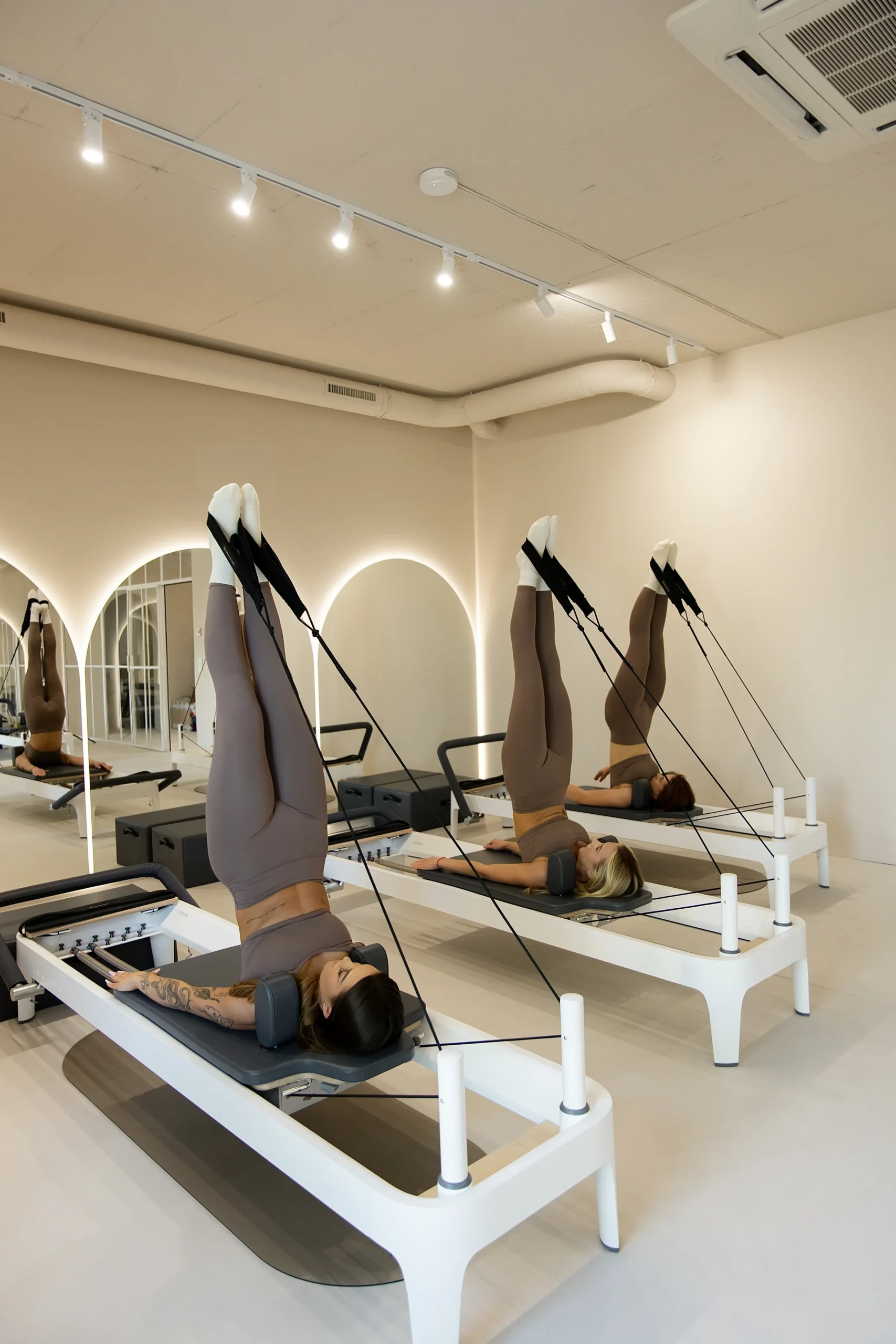 Reformer ustawiony w eleganckim studiu pilates z łukowymi przejściami i lustrami. Przestrzeń jest jasna, minimalistyczna i przygotowana do treningów indywidualnych.